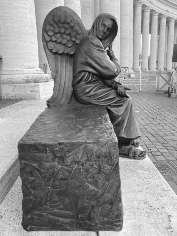 Schwarz-weiße Statue eines sitzenden Engels vor einer Säulenreihe.